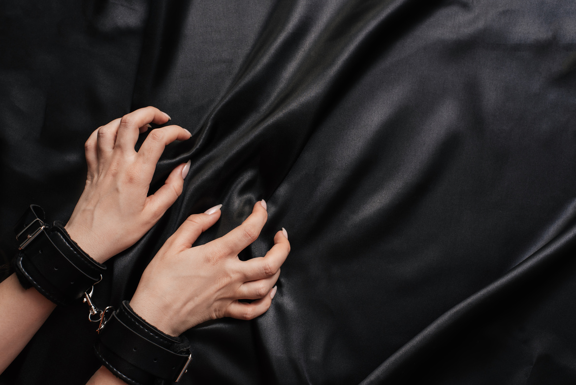 Female Hands in Handcuffs on a Dark Silk Sheet