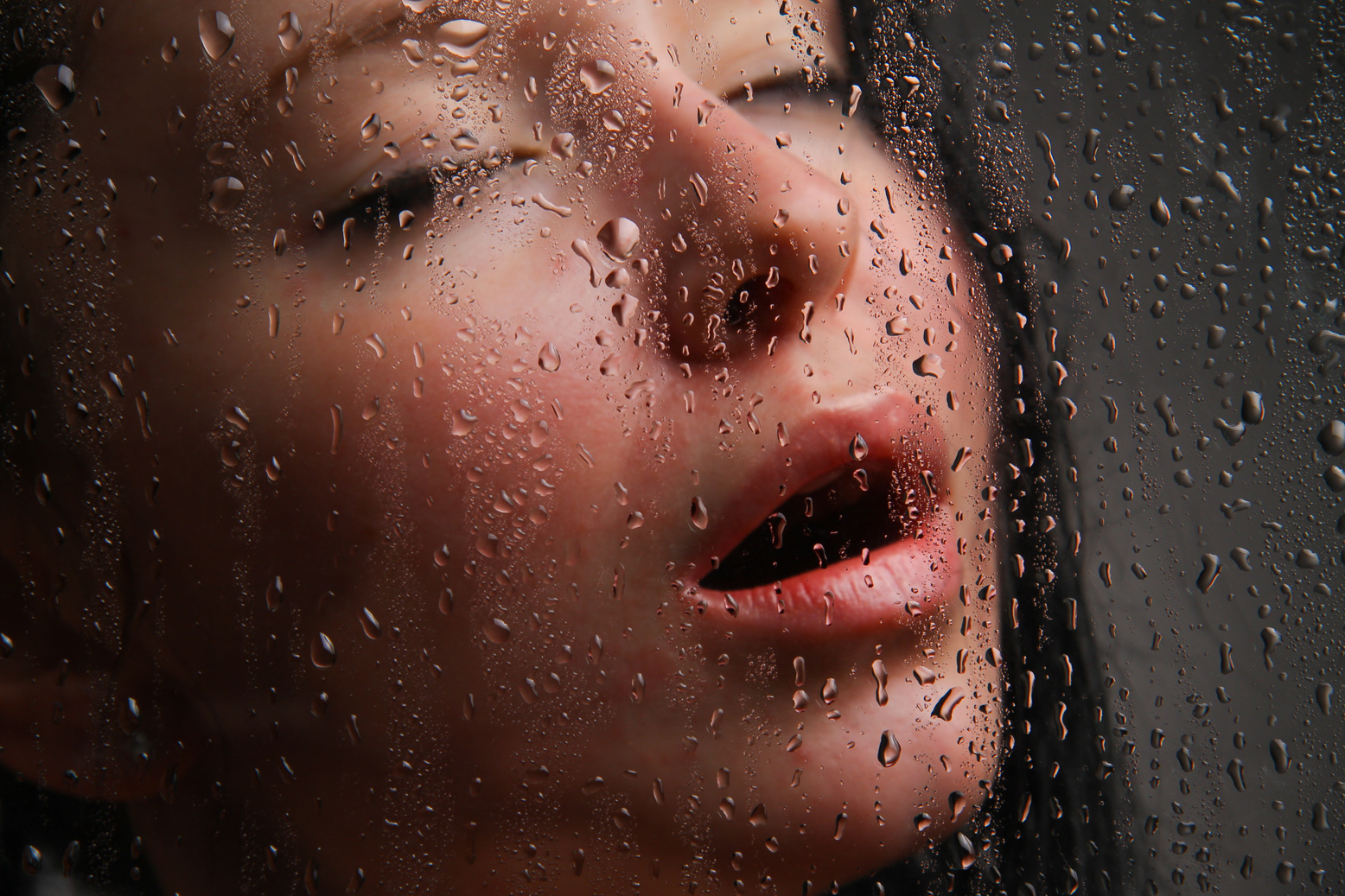Girl with her mouth open behind wet glass